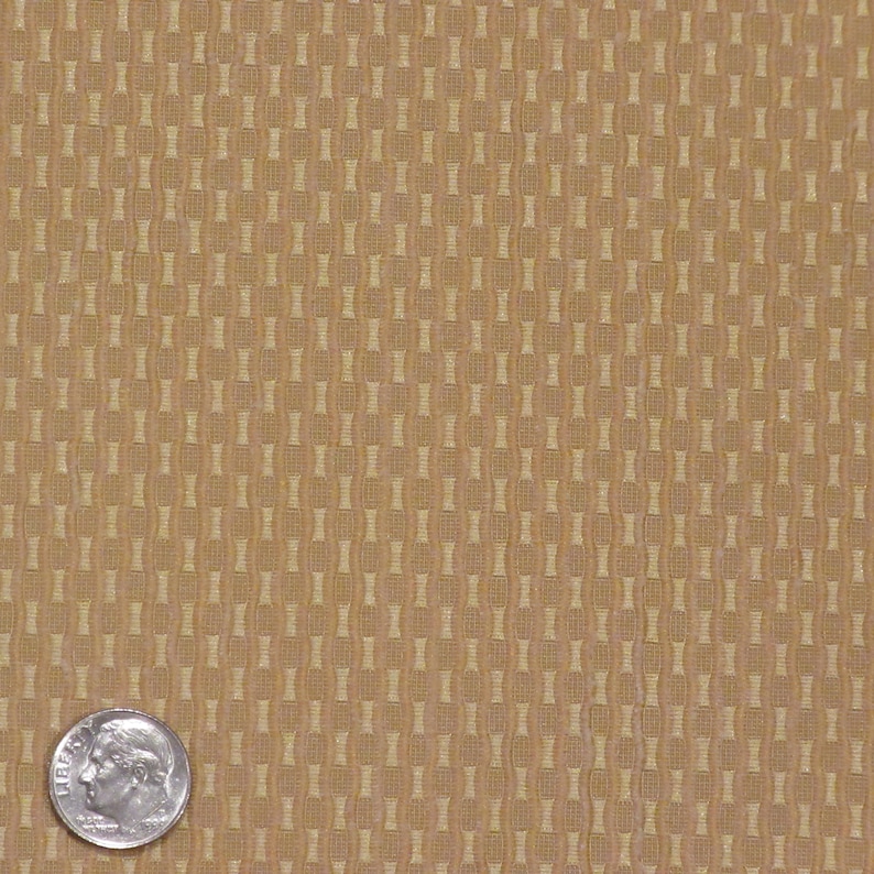 May include: Close-up of a tan fabric with a repeating pattern of vertical columns of connected shapes. A U.S. dime is in the lower left corner for scale, showing the texture and scale of the fabric.