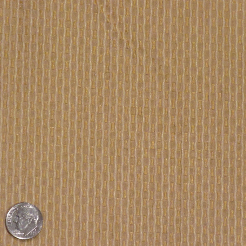May include: Close-up of a tan fabric with a repeating vertical pattern. The pattern consists of elongated, interconnected shapes in a lighter shade of tan, creating a textured appearance. A U.S. dime is in the lower left corner for scale.
