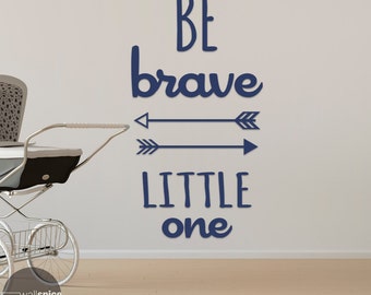 May include: A navy blue wall decal with the text "Be brave little one" and two arrows. The decal is on a white wall next to a white baby stroller.