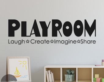 Pode incluir: Adesivo de parede preto e branco "Playroom" com as palavras "Laugh, Create, Imagine, Share" abaixo. O adesivo está em uma parede cinza claro acima de uma estante branca com brinquedos e livros.