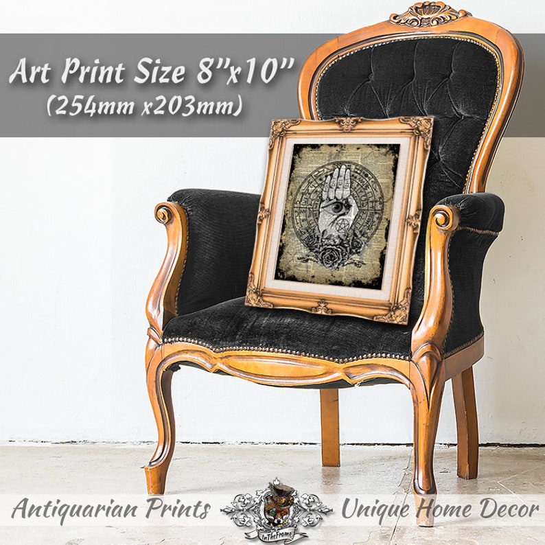 Puede incluir: Una impresi&oacute;n de arte enmarcada con una est&eacute;tica vintage que presenta una mano con un ojo en la palma, rodeada de rosas y un dise&ntilde;o circular. La impresi&oacute;n mide 20,3 cm por 25,4 cm y se muestra en una silla de terciopelo negro.