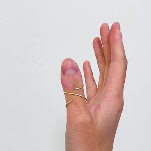 May include: A gold ring with a twisted design worn on a person's thumb.