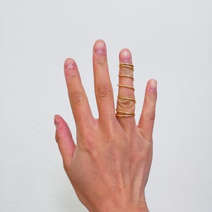 May include: A hand wearing a stack of five gold rings on the middle finger.