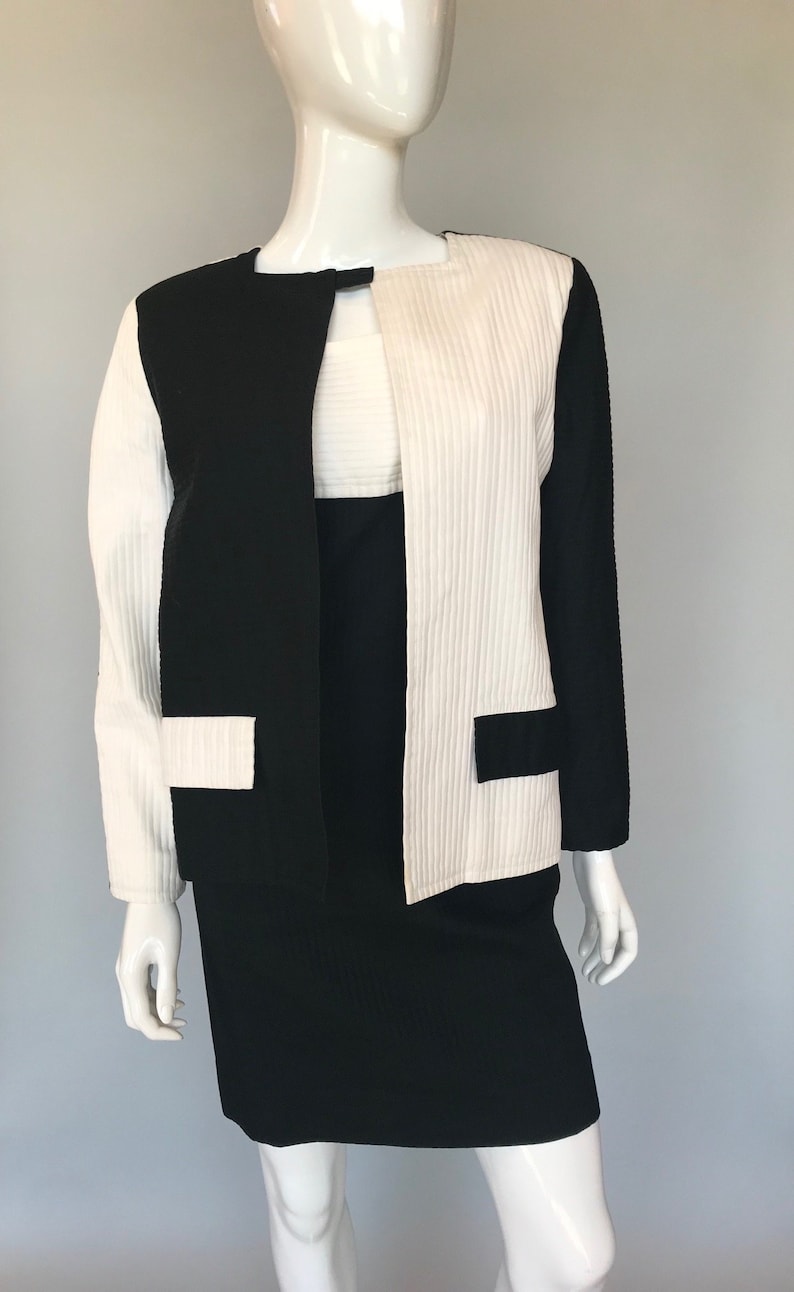 May include: A black and white dress suit with a skirt and a jacket. The jacket has a white panel down the center front and black panels on the sides. The skirt is black.