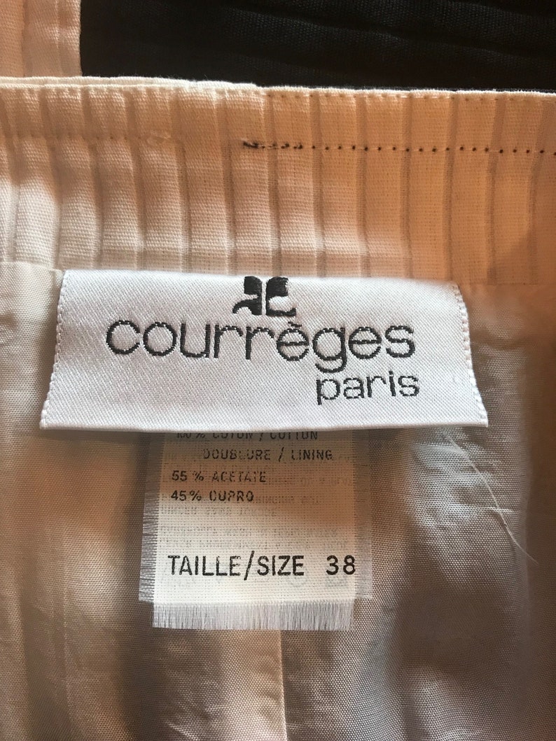 May include: White clothing label with black text that reads "courr&egrave;ges paris". The label also includes the text "DOUBLURE / LINING", "55% ACETATE", "45% CUPRO", and "TAILLE/SIZE 38".