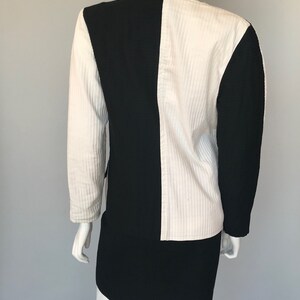 May include: A black and white jacket and skirt set. The jacket is made of a textured fabric and has a contrasting color block design. The skirt is a simple, straight skirt.