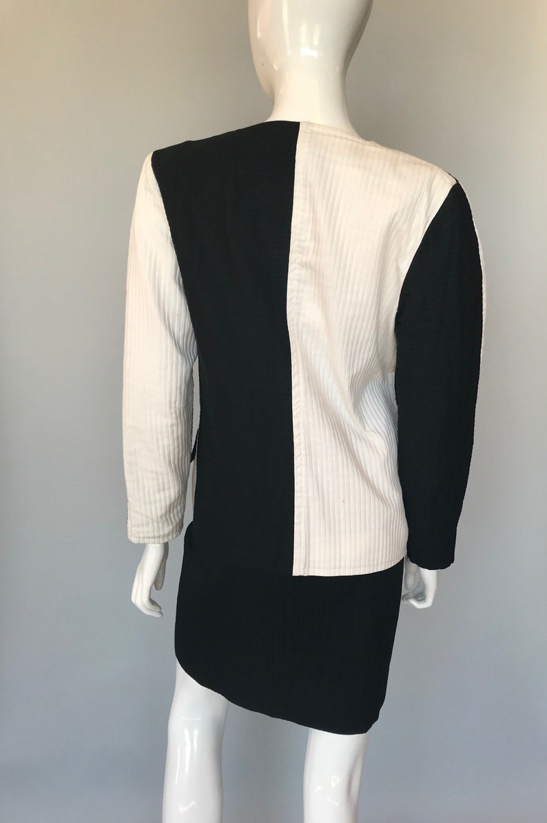 May include: A black and white jacket and skirt set. The jacket is made of a textured fabric and has a contrasting color block design. The skirt is a simple, straight skirt.