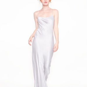 May include: A woman wearing a long, silver satin slip dress. The dress has a scoop neck and thin straps.