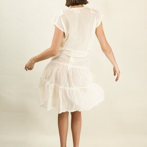May include: A white crochet dress with a tiered skirt and a mesh top. The dress is worn by a person with short brown hair. The person is wearing teal platform heels.