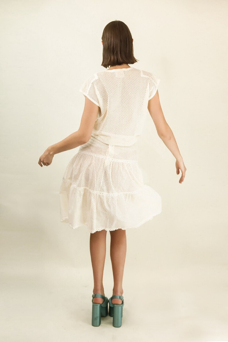 May include: A white crochet dress with a tiered skirt and a mesh top. The dress is worn by a person with short brown hair. The person is wearing teal platform heels.