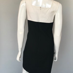 May include: A sleeveless dress with a white top and black bottom. The dress has a square neckline and a fitted silhouette.