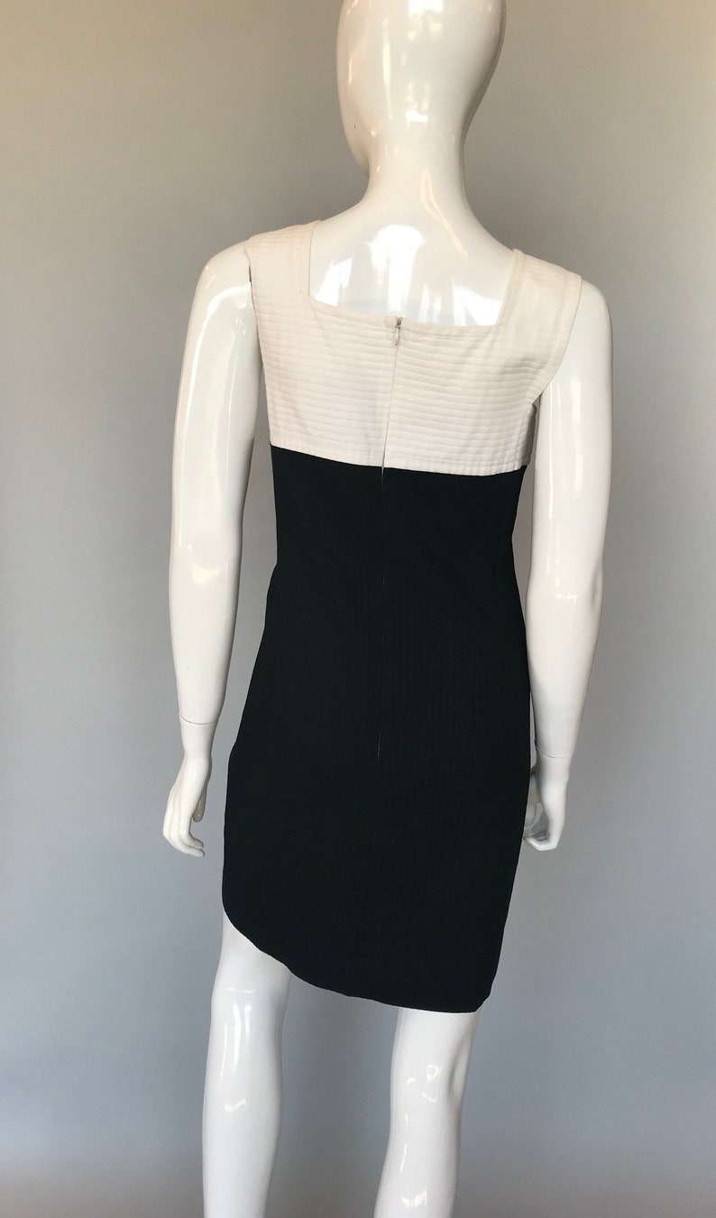 May include: A sleeveless dress with a white top and black bottom. The dress has a square neckline and a fitted silhouette.