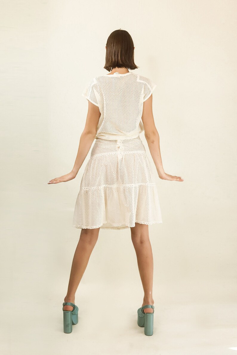 May include: A white crochet dress with a tiered skirt and a fitted bodice. The dress is made of a lightweight, breathable fabric and has a relaxed fit. The model is wearing the dress with a pair of teal platform heels.