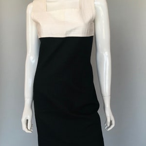May include: A sleeveless dress with a white top and a black bottom. The dress has a square neckline and a fitted silhouette.