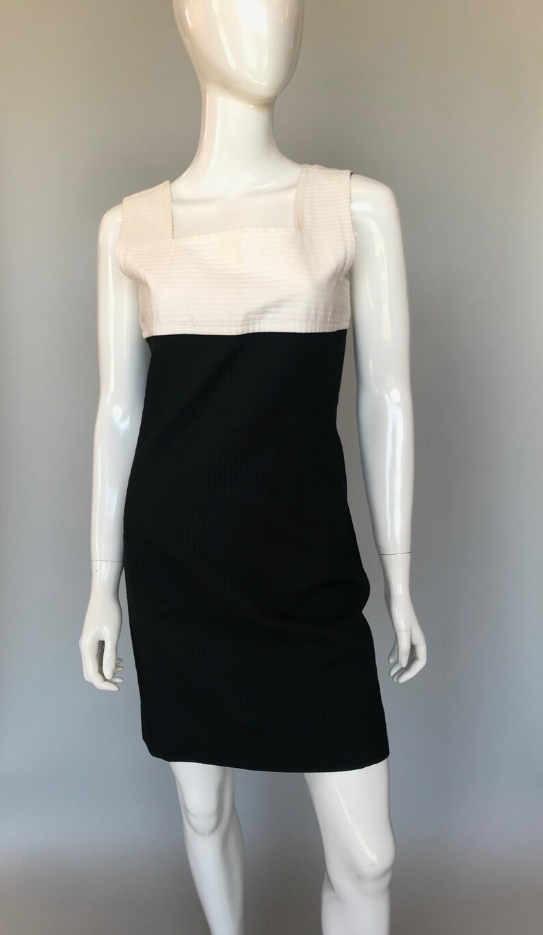 May include: A sleeveless dress with a white top and a black bottom. The dress has a square neckline and a fitted silhouette.