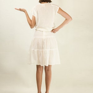 May include: A white, tiered skirt with a lace overlay and a matching white crochet top. The model is wearing teal platform heels.