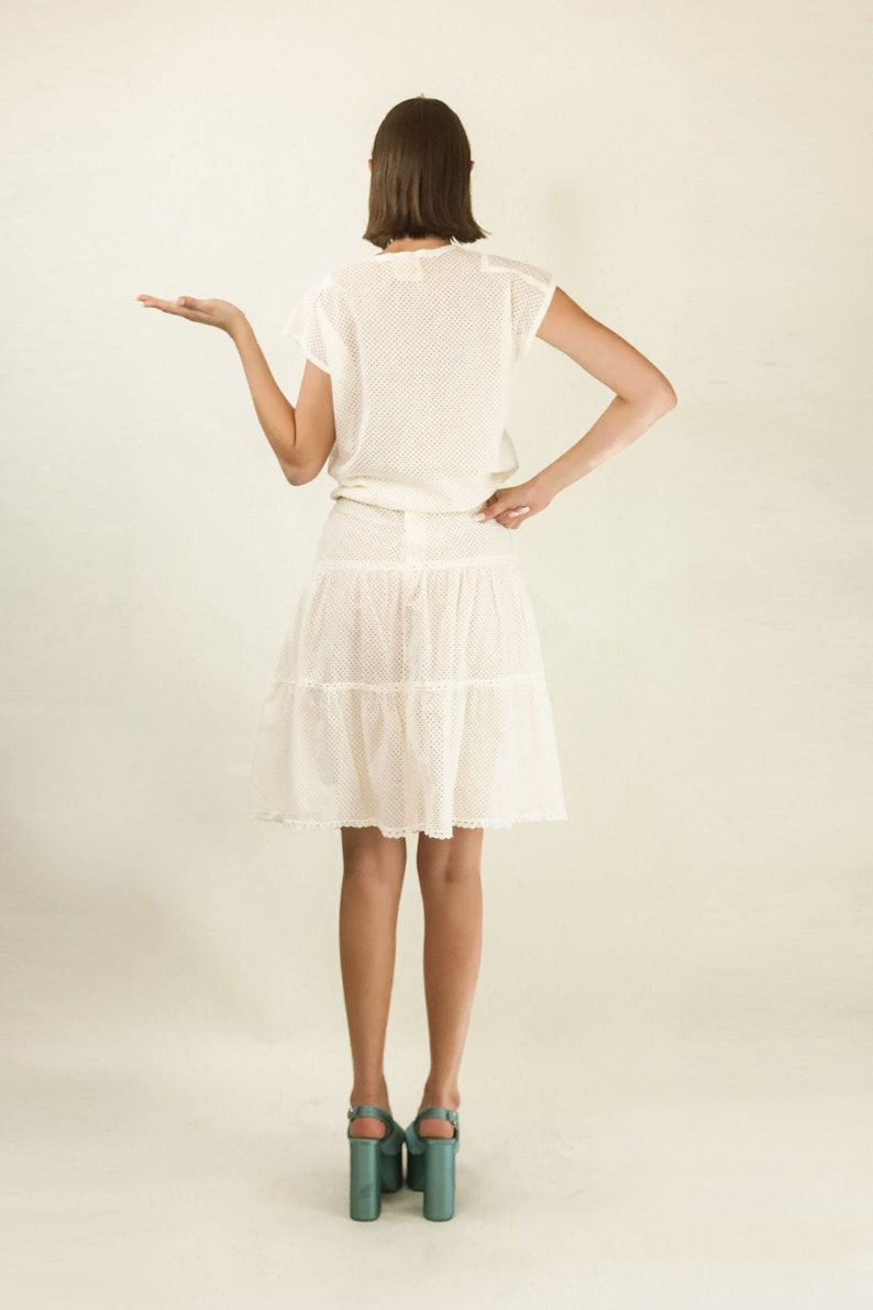 May include: A white, tiered skirt with a lace overlay and a matching white crochet top. The model is wearing teal platform heels.