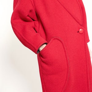 May include: A red wool coat with a single button closure and a unique curved pocket design.
