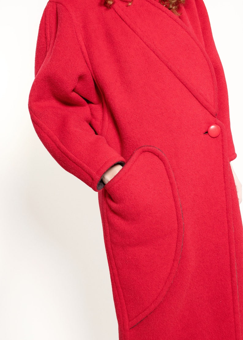 May include: A red wool coat with a single button closure and a unique curved pocket design.