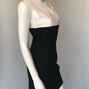 May include: A sleeveless black and white dress with a fitted silhouette. The top half of the dress is white with a textured fabric and the bottom half is black.