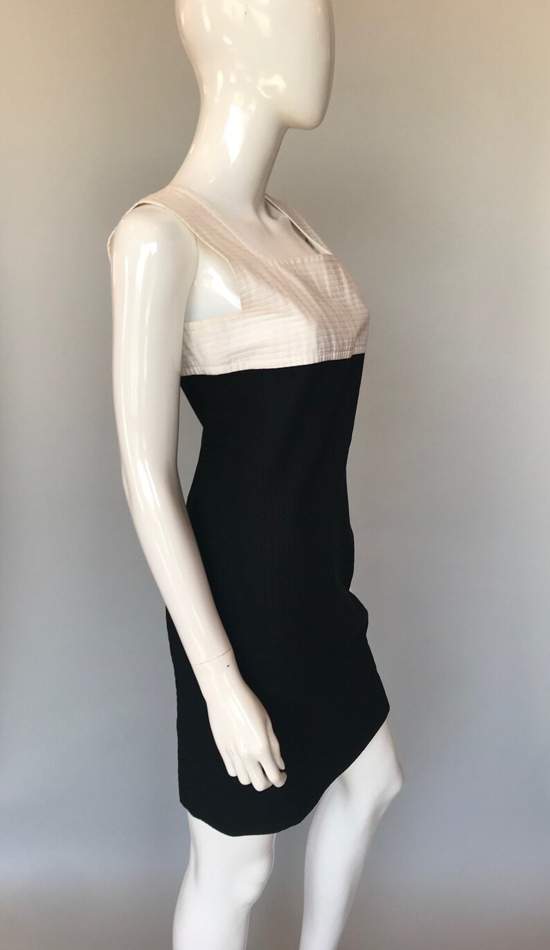 May include: A sleeveless black and white dress with a fitted silhouette. The top half of the dress is white with a textured fabric and the bottom half is black.