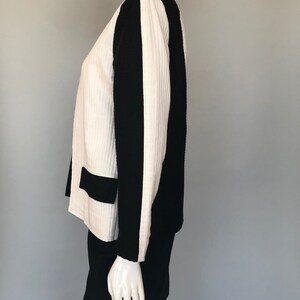 May include: A white and black skirt suit with a ribbed texture. The jacket has a black panel down the side of each sleeve. The skirt is a simple A-line style.