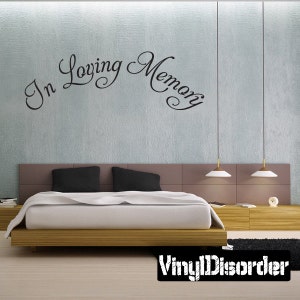 May include: A black vinyl wall decal with the text "In Loving Memory" in a cursive font. The decal is displayed on a light gray wall above a bed with black bedding.