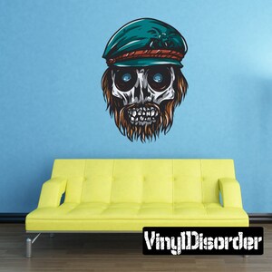 May include: A skull wearing a green and red cap with a beard. The skull has large, white eyes and a toothy grin. The background is a light blue wall.