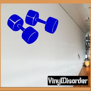 Può includere: Due manubri blu sono mostrati su una parete bianca. I manubri sono in posizione diagonale, con il manubrio superiore che si sovrappone leggermente a quello inferiore. I manubri sono un design semplice a silhouette.