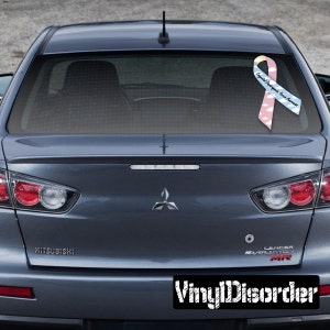 May include: A blue car with a pink and blue ribbon sticker on the back window. The ribbon has a white cloud pattern and the text "Epilepsy Awareness" on it. The car has a "Mitsubishi" logo on the back.
