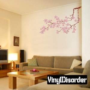 May include: A living room with a light brown couch and a coffee table. A pink cherry blossom branch wall decal is on the wall behind the couch. The decal is from Vinyl Disorder.