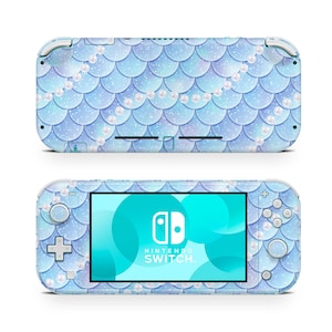 May include: A light blue Nintendo Switch Lite console with a mermaid scale design and pearl accents. The console has a turquoise screen with the Nintendo Switch logo and text.