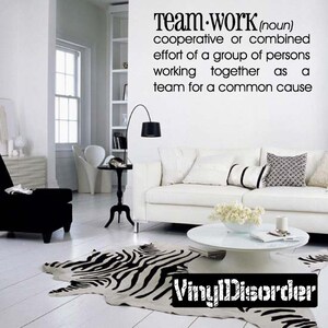 May include: A white couch with pillows in a living room setting. A zebra print rug is on the floor in front of the couch. The wall has a black and white vinyl decal with the definition of the word "teamwork".