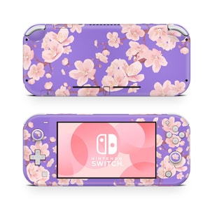 Puede incluir: Una consola Nintendo Switch Lite morada con un diseño de flores de cerezo rosas. La consola tiene un borde blanco y una pantalla blanca con el logotipo y el texto de Nintendo Switch.