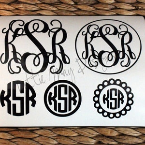 May include: A sheet of white vinyl with four black monogram decals. The monograms are in different styles, including a script font, a block font, and a font with a decorative border. The monograms all spell "KSR".