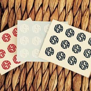 May include: Three sheets of paper with circles printed on them. The circles have the letters "USA" inside them. The circles on the left sheet are red, the circles on the middle sheet are white, and the circles on the right sheet are blue.