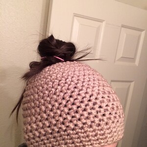 May include: A light brown crochet beanie hat. The hat has a textured stitch pattern and is worn on the head. The hat is a neutral colour and appears to be warm and comfortable, suitable for cooler weather.