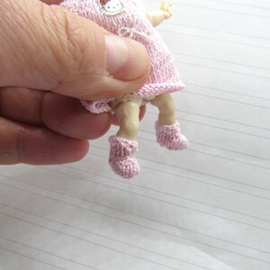 K&ouml;nnte beinhalten: Eine kleine rosa gestrickte Puppe mit einem Hello-Kitty-Motiv auf dem Kleid. Die Puppe tr&auml;gt rosa gestrickte Stiefelchen.