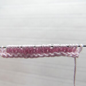K&ouml;nnte beinhalten: Nahaufnahme eines rosa gestrickten Stoffes auf einer Stricknadel. Der Stoff wird bearbeitet und das Garn h&auml;ngt an der Nadel.