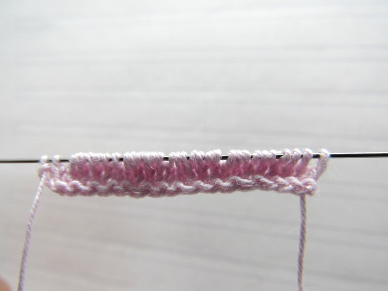 K&ouml;nnte beinhalten: Nahaufnahme eines rosa gestrickten Stoffes auf einer Stricknadel. Der Stoff wird bearbeitet und das Garn h&auml;ngt an der Nadel.