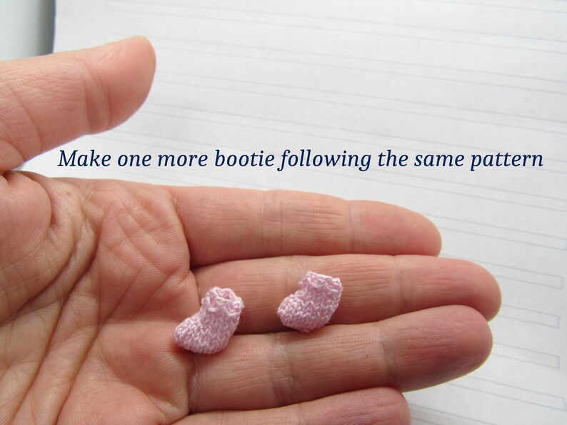 K&ouml;nnte beinhalten: Zwei rosa gestrickte Babyschuhe, einer in jeder Hand. Der Text "Make one more bootie following the same pattern" ist &uuml;ber den H&auml;nden sichtbar.