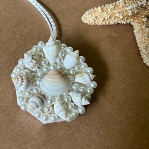 May include: A white pendant necklace with a hexagonal charm featuring a cluster of small white seashells and faux pearls.