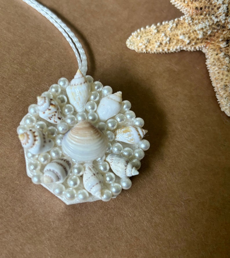 May include: A white pendant necklace with a hexagonal charm featuring a cluster of small white seashells and faux pearls.