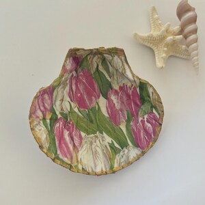 May include: A decorative seashell with a pink and white tulip design. The shell is trimmed with gold paint.