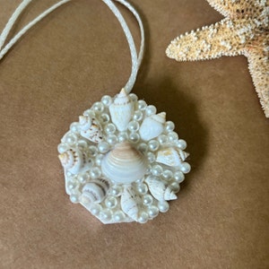 May include: A white pendant necklace with a circular charm featuring a cluster of small white seashells and pearls.