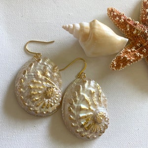 May include: A pair of gold earrings featuring iridescent abalone shell with gold accents. The earrings are a unique and elegant piece of jewelry.