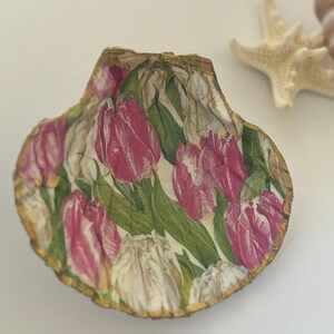 May include: A seashell with a gold trim, decorated with a pink and white tulip floral pattern.