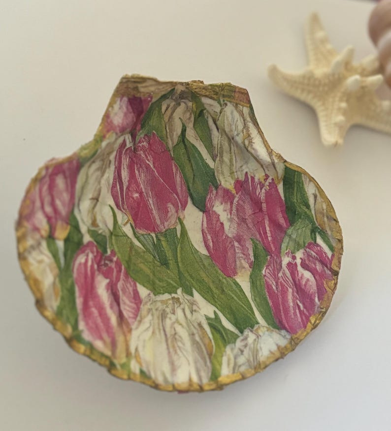 May include: A seashell with a gold trim, decorated with a pink and white tulip floral pattern.