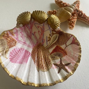 May include: A white seashell dish with a pink and gold floral design. The dish is decorated with gold seashells, pearls, and a starfish.