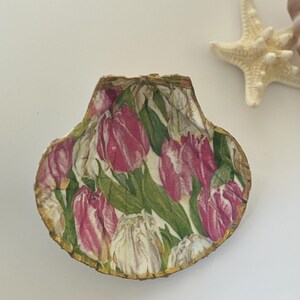 May include: A seashell with a gold trim, decorated with a pink and white floral pattern of tulips.